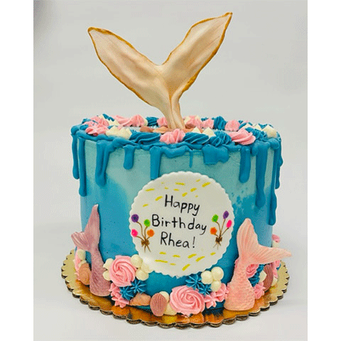 a singled tier cake with two tone aqua blue icing with blue icing dripping down the sides from the top of the cake. Along the base of the cake has mermaid tailes sticking up from the bottom, with pint swirled flowers, blue star fish, brown sea-shells and white pearls. On the tope of the cake has pink swirl flowers, blue star fish, whit pearls and a fin from a mermaids tail